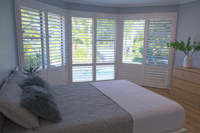 White plantation shutters covering a large bay window in a bright master bedroom